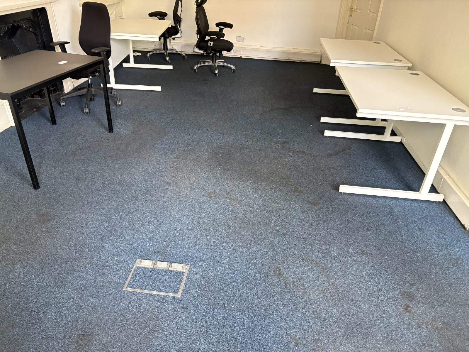 Blue office carpet before cleaning, with dark traffic marks and spill stains spreading across the floor between the desks