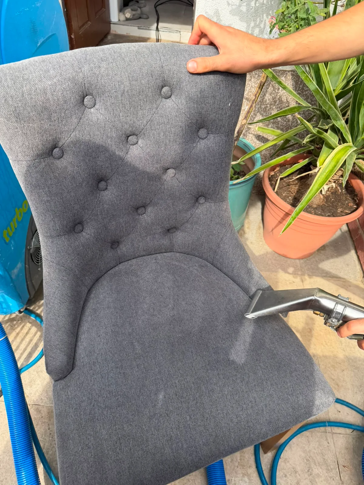 The same chair back part-way through hot-water extraction — the hand tool is still on the fabric and the cleaned section is dark with moisture, not yet dry
