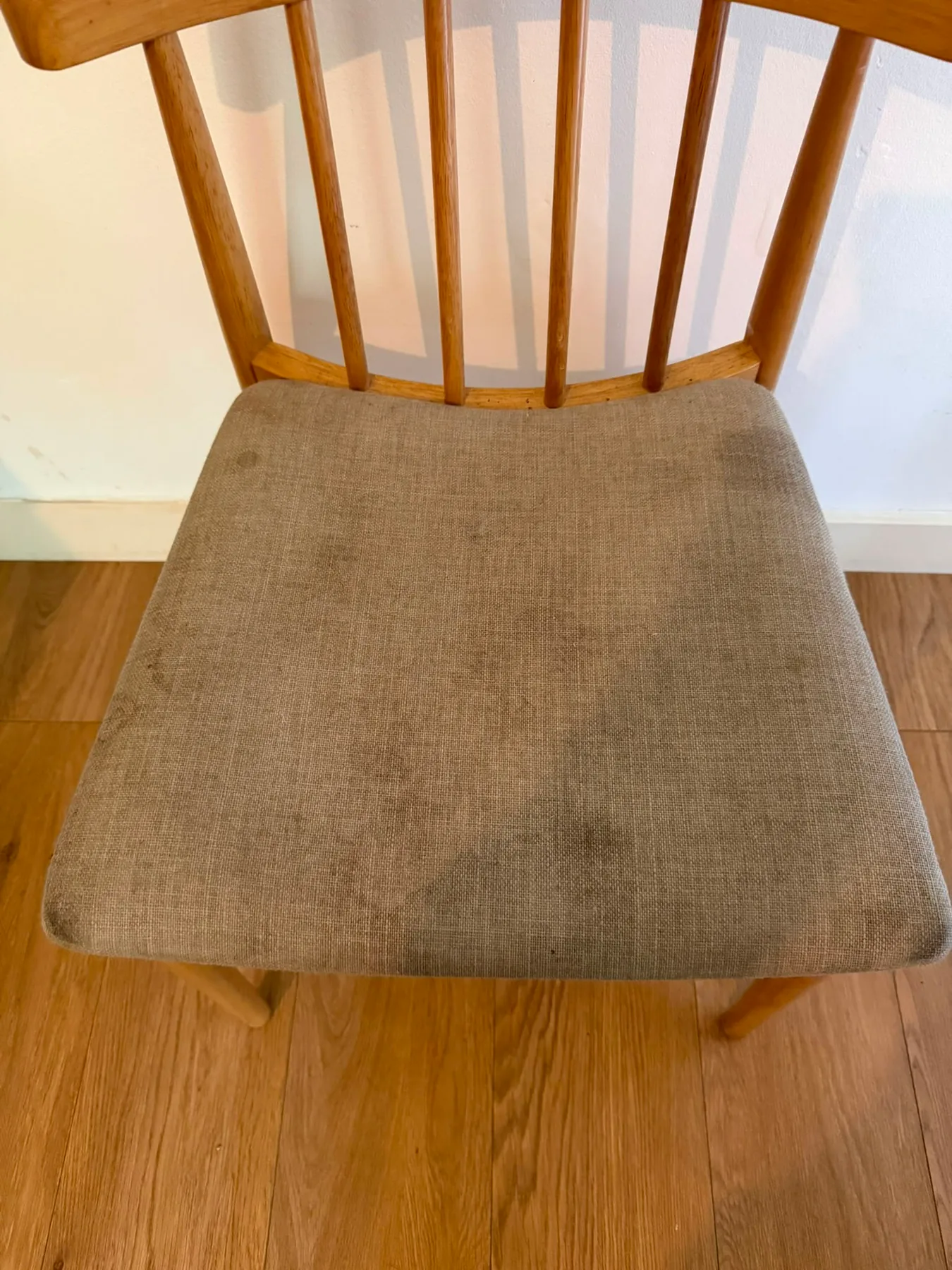 A wooden dining chair with a beige linen seat pad before cleaning, dark soiling spread across the middle of the pad