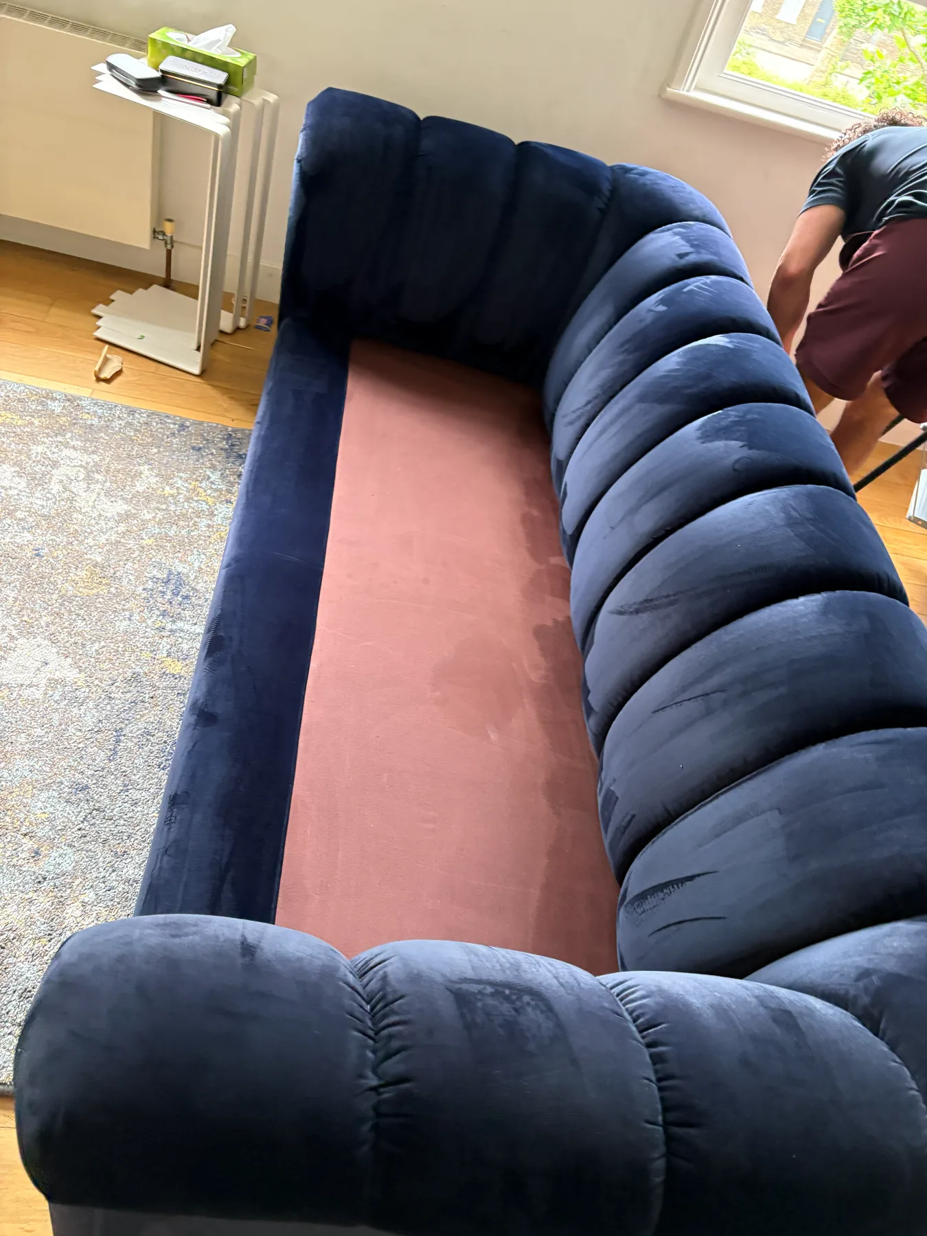 A navy velvet sofa with its seat cushions removed, part-way through cleaning, the bare deck exposed