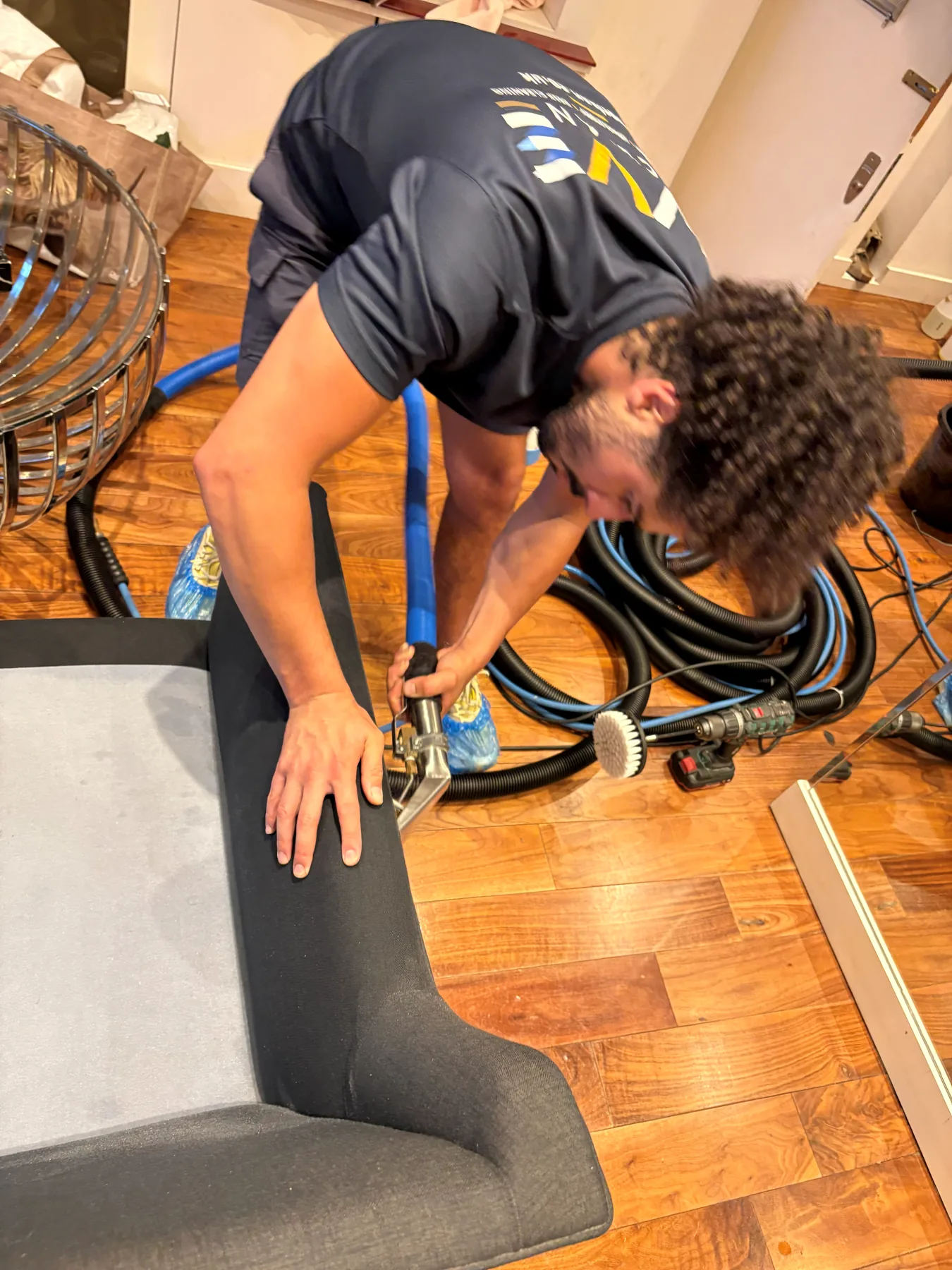 A technician drawing a hand extraction tool along the edge of a dark grey seat, machine hoses coiled on the floor behind