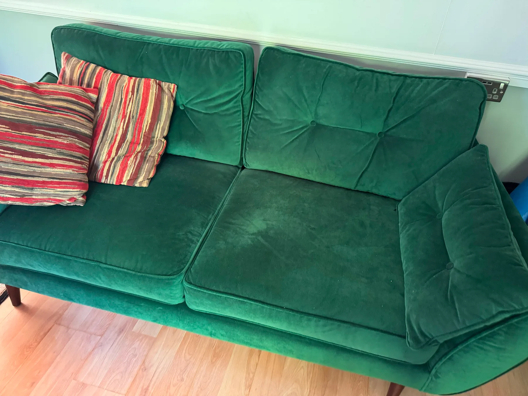 A deep green velvet sofa with striped scatter cushions, the pile brushed even after cleaning