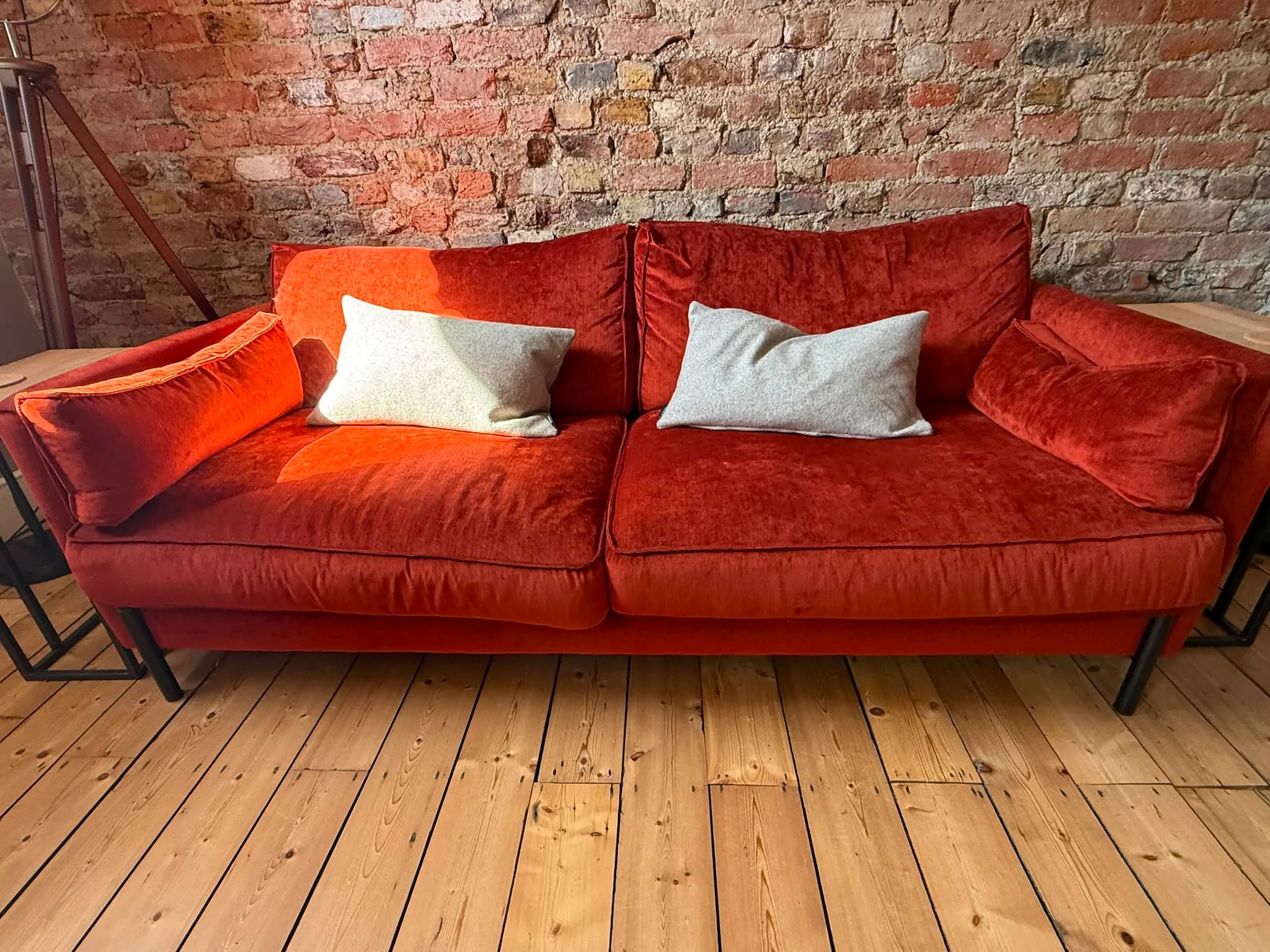 A rust-red velvet sofa on a stripped pine floor against an exposed brick wall, photographed after cleaning