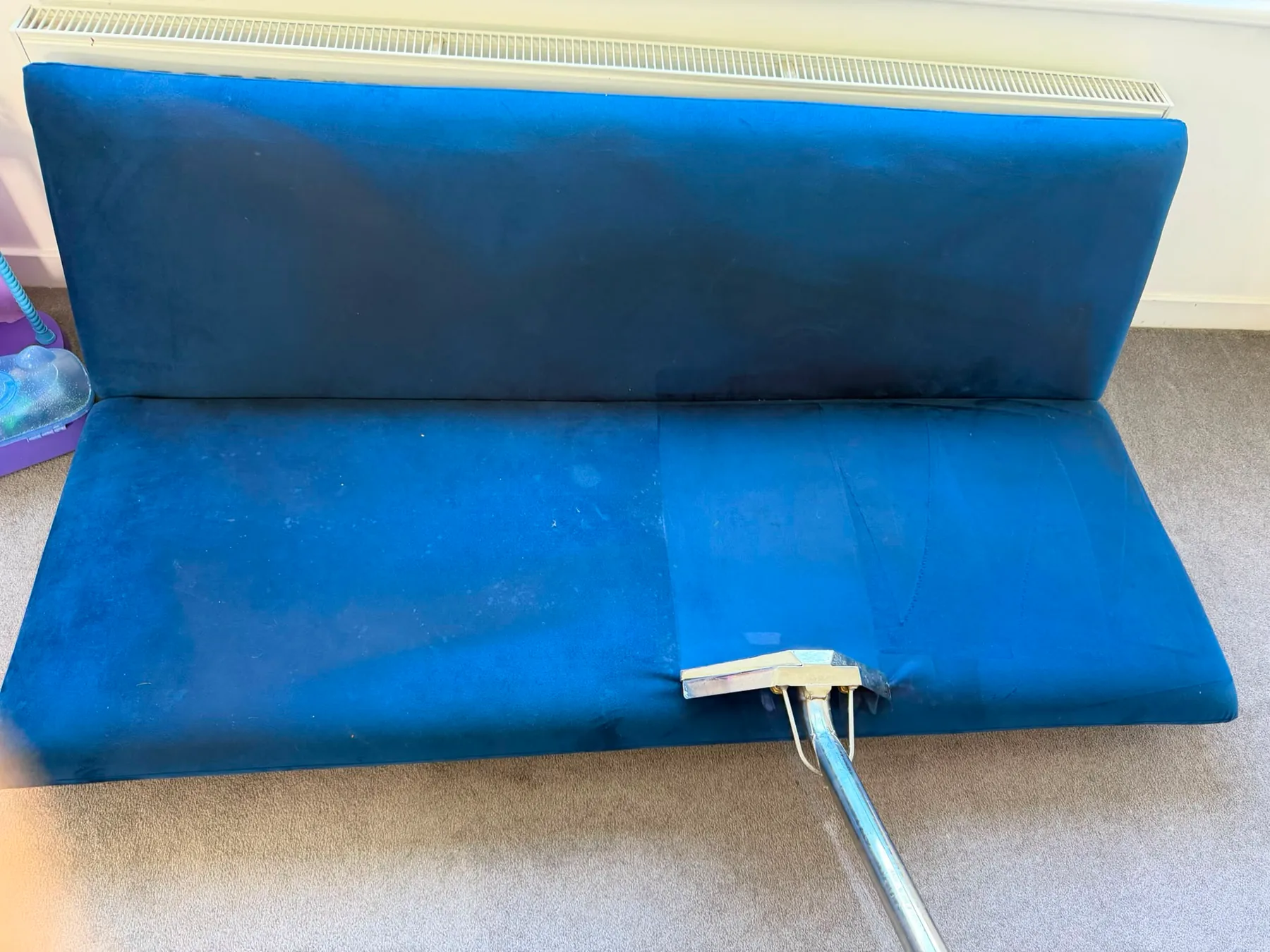 A blue velvet bench seat and back being cleaned, the extraction tool part-way across the seat leaving a darker wet band